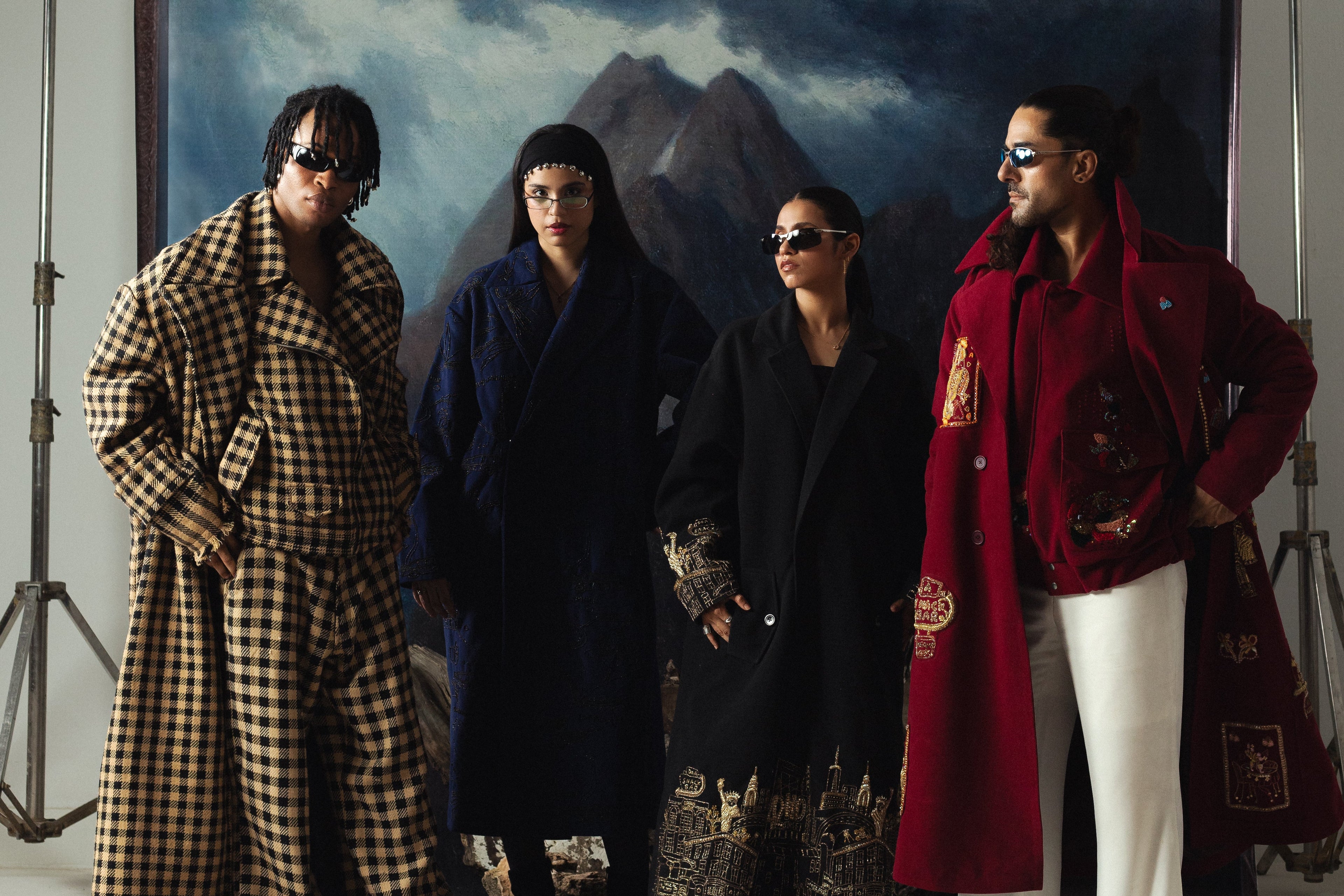 Four individuals in stylish outfits standing in front of a scenic painting.
